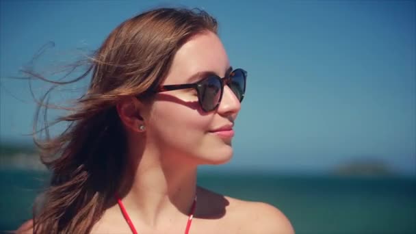Fermer Portrait d'une belle brune mignonne européenne Jeune femme ou fille joyeuse souriante regardant la caméra, courant à travers les cheveux soufflant dans le vent sur la plage tropicale, ralenti
. - Séquence, vidéo