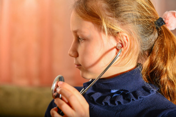 Une fille tient un stéthoscope dans ses mains et écoute le patient, jeu à domicile chez le médecin
. - Photo, image