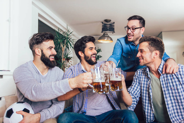 Men watching sport on tv together at home screaming cheerful. Group of friends sitting on the couch and watching a football game. - Foto, Imagem