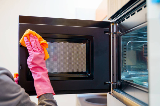 Imagem de mãos de mulher em luvas de borracha lavar microondas
. - Foto, Imagem