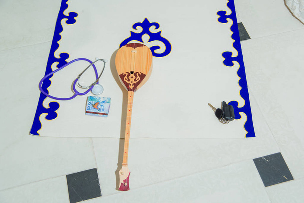Estera nacional kazaja para los primeros pasos del bebé. El tapete es blanco con un adorno nacional kazajo. La textura de la tela. Instrumento musical kazajo dombra
. - Foto, imagen