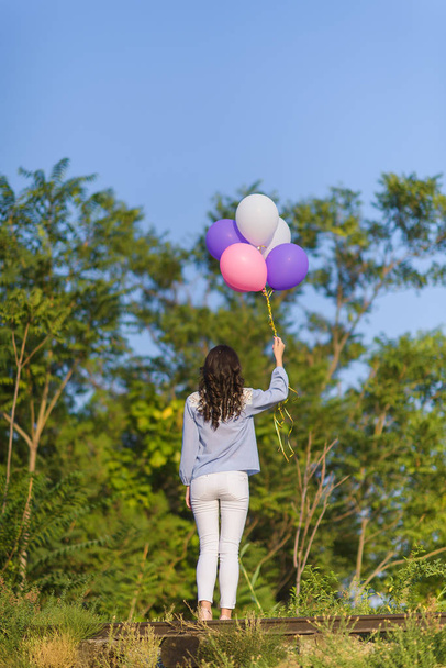 A walk in the Park. The girl with the balloons. Balloons pink and purple. Nature. Trees with green leaves. Helium balloons. - Foto, afbeelding