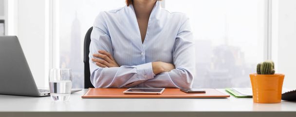 Empresária americana confiante sentada à mesa em seu escritório e posando com os braços cruzados
 - Foto, Imagem