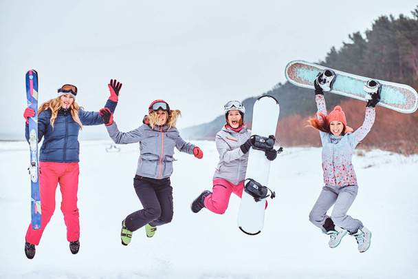 Cheerful women friends in sports winter clothes with snowboards and skis posing  - Photo, Image
