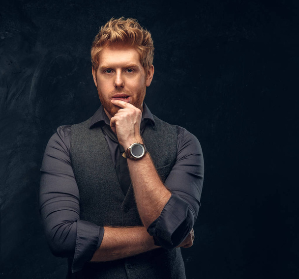 Elegantly dressed redhead man posing with thoughtful look in studio against a dark textured wall - Photo, Image