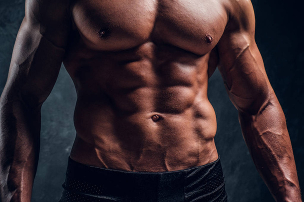 Close-up image of muscular torso with dark wall background - Foto, Bild