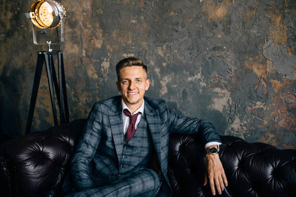 Retrato de un hombre de negocios guapo en traje en un sofá de cuero vintage de lujo
 - Foto, imagen