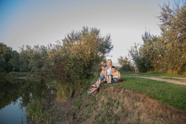 2 人の息子と幸せな美しい家庭が夕暮れ自然湖の近くに座っています。 - 写真・画像