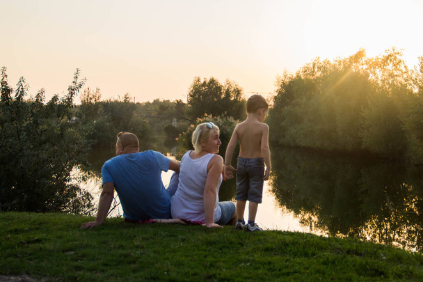 Šťastná rodina sedí u jezera a pozorujte západ slunce - Fotografie, Obrázek