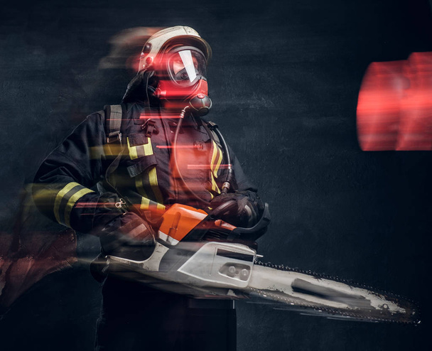A tűzoltó-bukósisak és oxigén maszk gazdaság egy láncfűrész portréja. Stúdió fotó egy sötét texturált falhoz - Fotó, kép