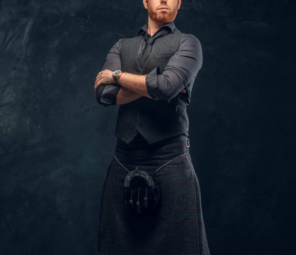 Kızıl saçlı adam kravat ve kollarını Studio bir karanlık dokulu duvara çarpı işareti ile poz İskoç eteği ile şık bir yelek giymiş - Fotoğraf, Görsel