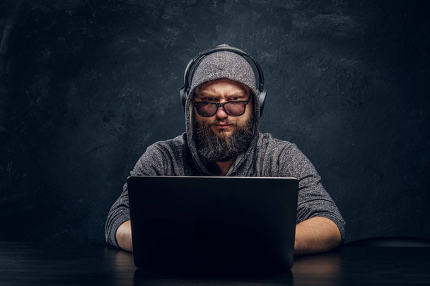 Hacker sedí za notebook v tmavé kanceláři a upřeně hledí na kameru - Fotografie, Obrázek