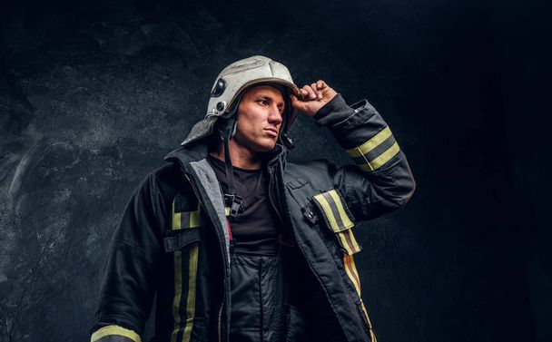 Statečný hasič v obleku oheň, pohled z boku a opravuje helmu s rukou - Fotografie, Obrázek