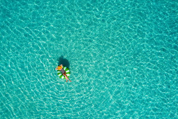 Aerial view of slim woman swimming on the swim ring  donut in the transparent turquoise sea in Seychelles. Summer seascape with girl, beautiful waves, colorful water. Top view from drone - Φωτογραφία, εικόνα