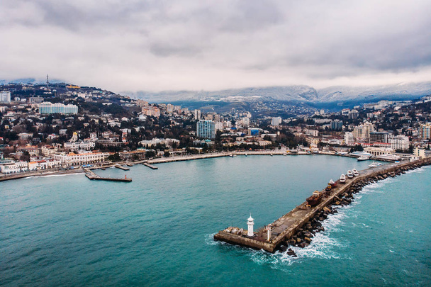 Luftaufnahme des Yalta-Dammes von der Drohne, alter Leuchtturm auf der Seebrücke, Küstenlandschaft und Stadtgebäude auf den Bergen, wunderschönes Winterpanorama des europäischen Urlaubsortes, Krim - Foto, Bild