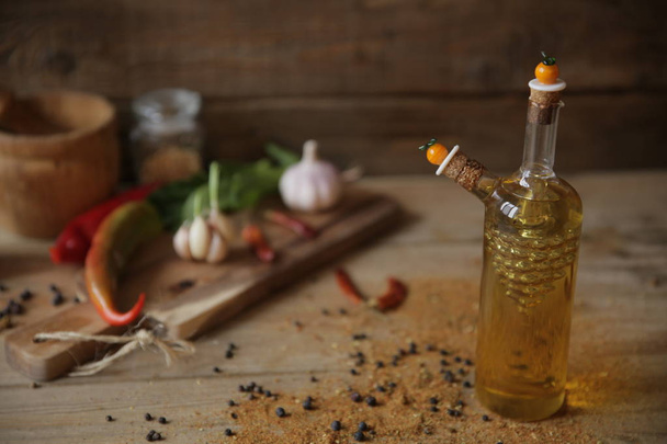 olive oil in a bottle on a wooden background with a wooden board with garlic, spices, dried pepper and herbs for decoration - Photo, Image