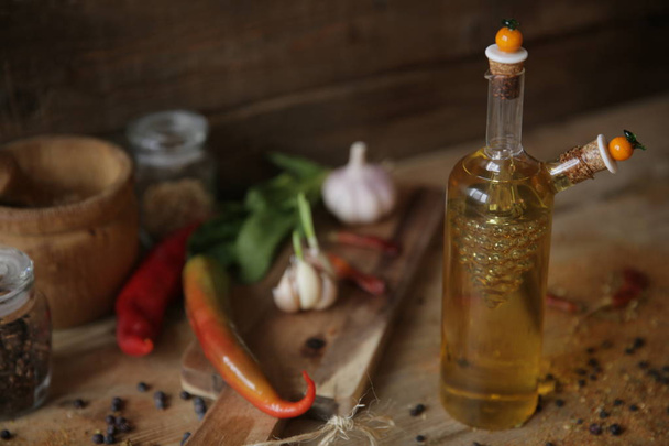 Olivenöl in einer Flasche auf einem hölzernen Hintergrund mit einem Holzbrett mit Knoblauch, Gewürzen, getrocknetem Pfeffer und Kräutern zur Dekoration - Foto, Bild