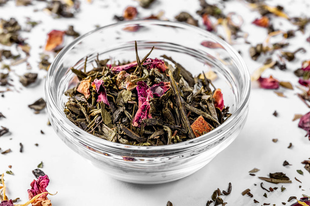 Green tea with dried flower petals and pieces of citrus on white background. Dried tea for welding. Diet and healthy drink - Фото, изображение