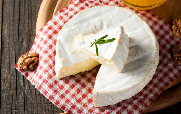 Brie típusú sajt. Camembert sajt. Friss sajt és egy szelet fából készült tábla dióval, mézzel és levelekkel. Olasz, francia sajt. - Fotó, kép