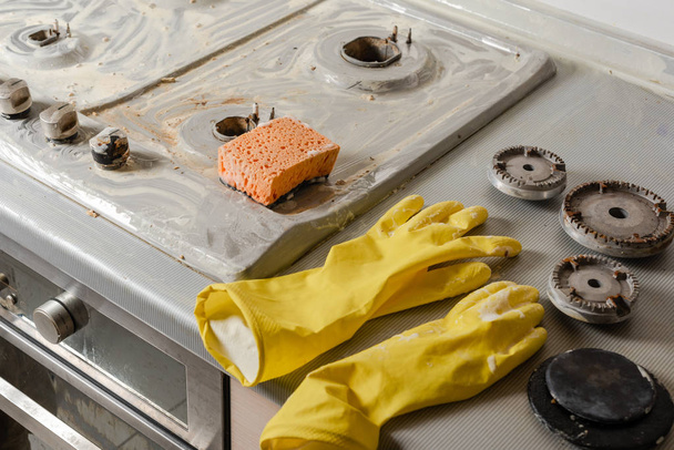 Brudnej gąbki pomarańczowy i żółty rękawice na kuchnia kuchenka. Proces czyszczenia z detergentem mydłem gazu zakres górze. - Zdjęcie, obraz