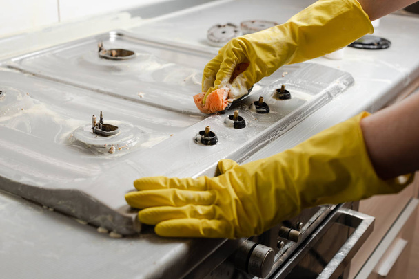 Hands of woman in yellow gloves cleaning gas cooker in kitchen. Detergent soap and foam on gas stove surface. - 写真・画像
