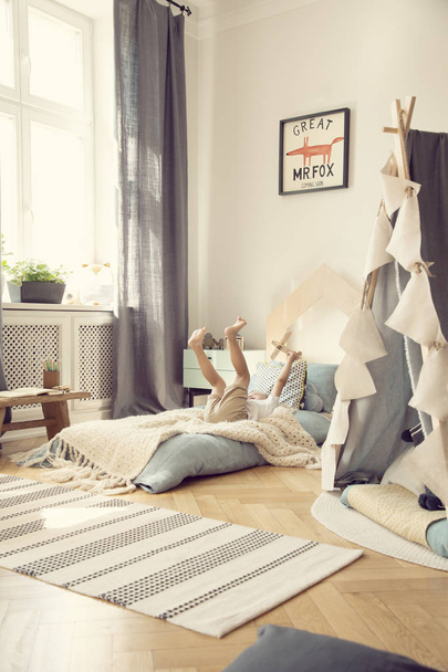 Kid with wooden aeroplane playing on blue bed in bright bedroom interior with tent and rug. Real photo - Fotoğraf, Görsel