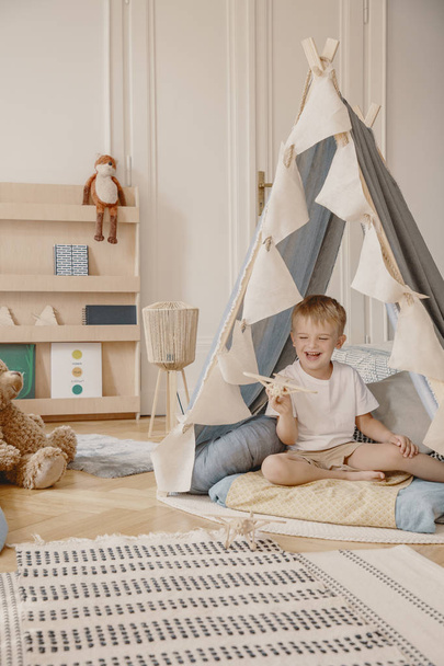 Cute little boy sitting in tent in stylish kid's playroom in modern apartment, real photo - Fotoğraf, Görsel