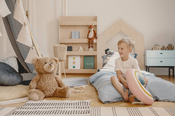 Cute child sitting on a bed in scandinavian kid's play room with toys, tent and wooden furniture - Foto, Imagem