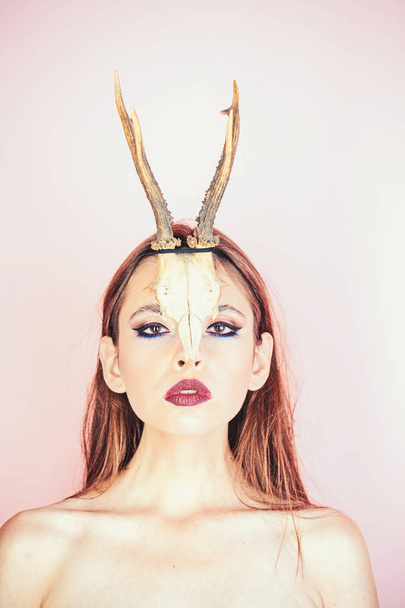 Beauty of woman with animal skull and antlers. Beauty look and cosmetics for skincare - Fotó, kép