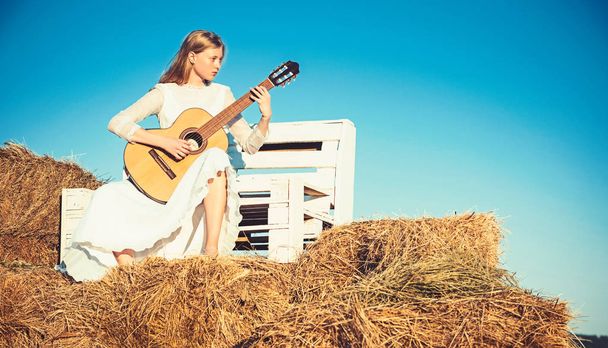 Albino girl hold acoustic guitar, string instrument. Sensual woman play guitar on wooden bench. Woman guitarist perform music concert. Fashion musician in white dress on sunny nature - Foto, imagen