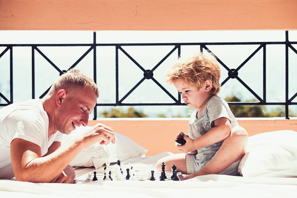 father with son on balcony play chess. Child play chess with father. Summer vacation of happy family. Family travel with kid on fathers day. Love and trust as family values - Foto, Imagen