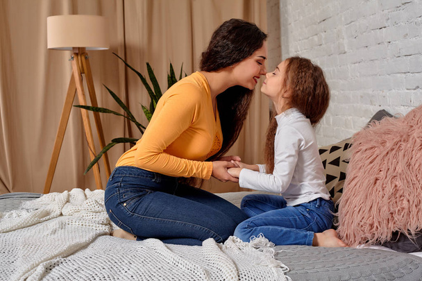 Love of young mother and daughter. They sit on the bed at home and have fun - Photo, Image