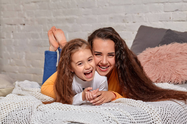 Love of young mother and daughter. They lie on the bed at home and have fun - Fotografie, Obrázek