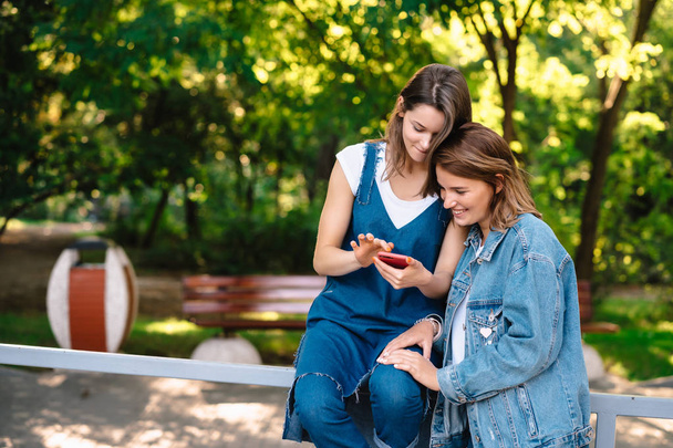 Smartphone vasıl belgili tanımlık bohça iki kadın kız bakmak - Fotoğraf, Görsel