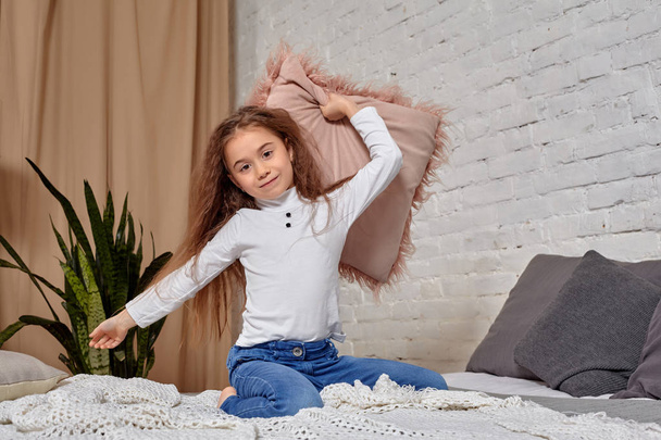Портрет очаровательной эмоциональной маленькой девочки на кровати, с подушкой
 - Фото, изображение