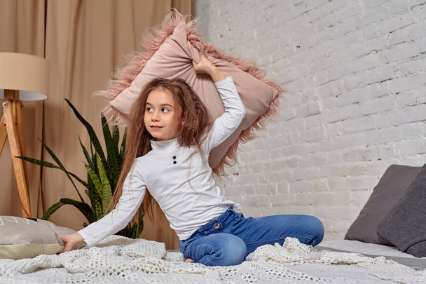 Portrait of adorable emotional little girl on the bed, with pillow - Фото, изображение