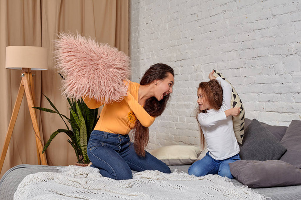 Jeune maman et fille s'amusent avec des combats d'oreillers sur le lit
 - Photo, image