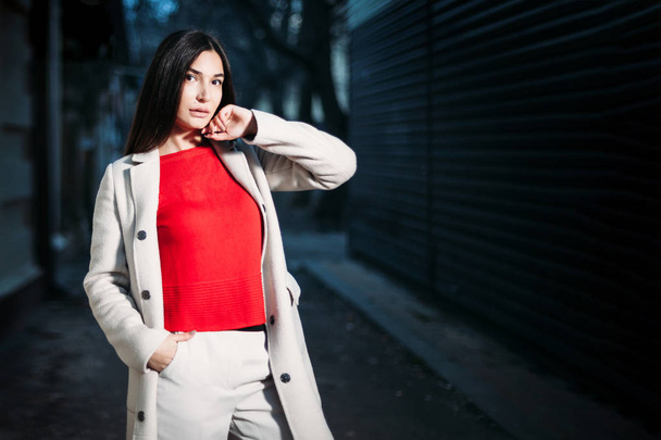 beautiful young brunette woman in red blouse white coat in evening outdoors - Foto, Imagem