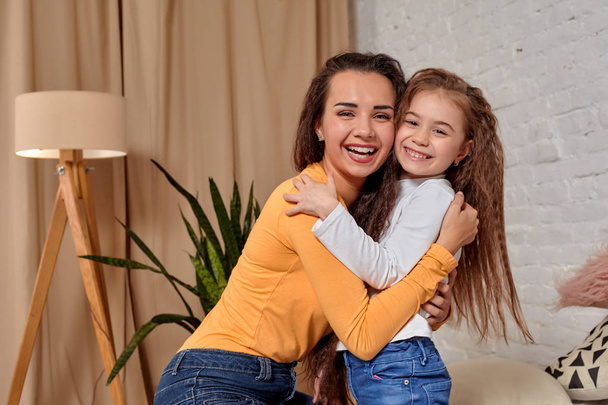 Love of young mother and daughter. They sit on the bed at home and have fun - Фото, изображение