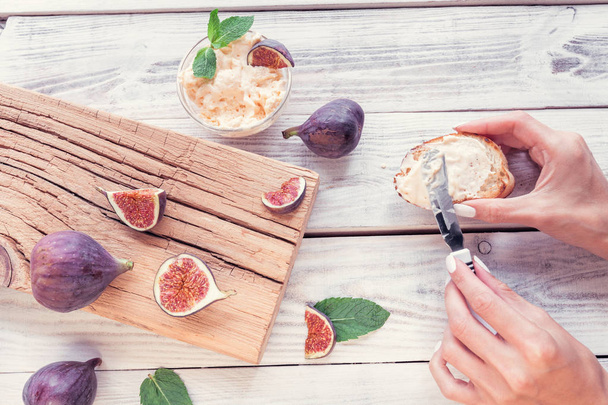 sliced figs and female hands grease a bread toaster by ricotta - Foto, afbeelding