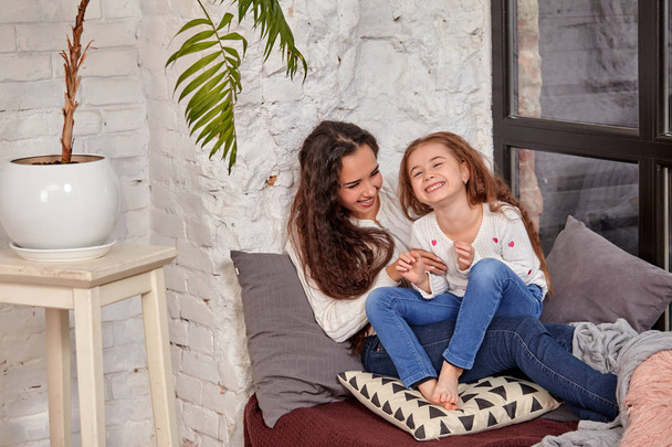 Mother and daughter sitting on sill near window in room - Foto, Bild