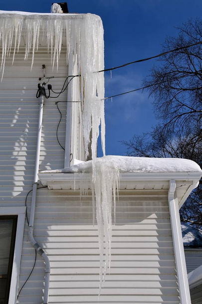 Massive icicles hang from a two story house which cover just about  two stories tall, - Photo, Image