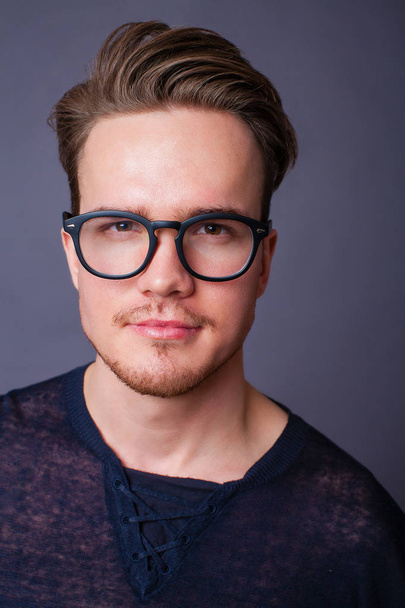 Studio portrait of a young man in big glasses on a dark background - Foto, Imagen