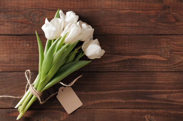Strauß von Tulpenblumen auf natürlichem Holztisch. Hochzeitsgrußkarte mit Kopierplatz, schöne Frühlingsblumen mit Anhänger - Foto, Bild