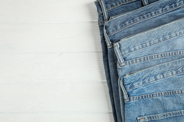 Different jeans folded on a white wooden background, space for text - Zdjęcie, obraz