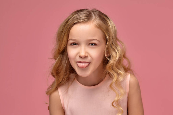 Маленька дівчинка з світлим кучерявим волоссям, в рожевій сукні позує для камери
 - Фото, зображення