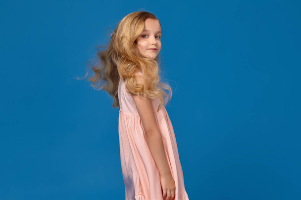 Fashionable little girl in a pink dress is posing on a blue background. - Foto, afbeelding