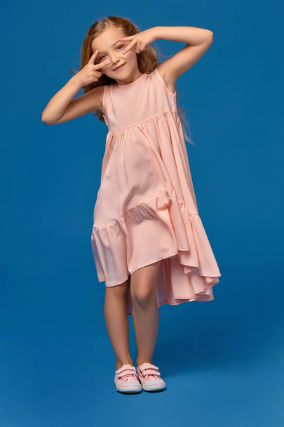 Модная маленькая девочка в розовом платье позирует на синем фоне
. - Фото, изображение