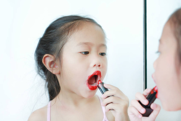 Adorable funny little girl applying lipstick over her mouth. - Zdjęcie, obraz