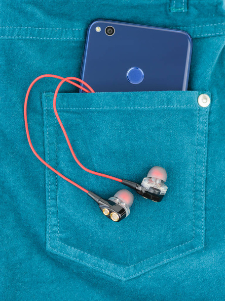Telefon jest w kieszeni zielone spodnie jeansowe z słuchawki. Koncepcja nowoczesnej mody dla urządzeń elektronicznych. - Zdjęcie, obraz